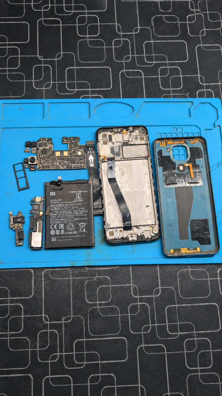 Phone opened with display and parts on a repair mat